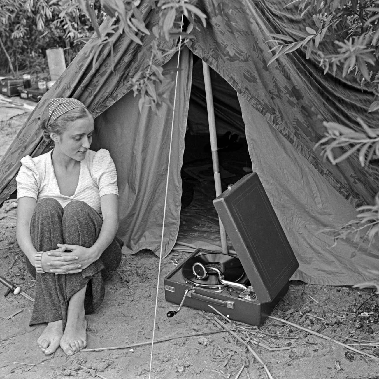 Young woman sitting and listening to a gramophone outside a tent.